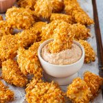 Chicken Nuggets auf einem Blech, serviert mit einem Dip, in dem ein Nugget eingetaucht wurde.