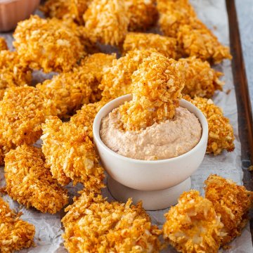 Chicken Nuggets auf einem Blech, serviert mit einem Dip, in dem ein Nugget eingetaucht wurde.