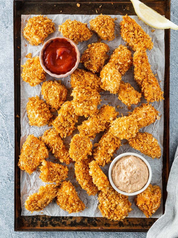 Knusprig gebackene Chicken Nuggets auf einem Blech mit zwei Dips.