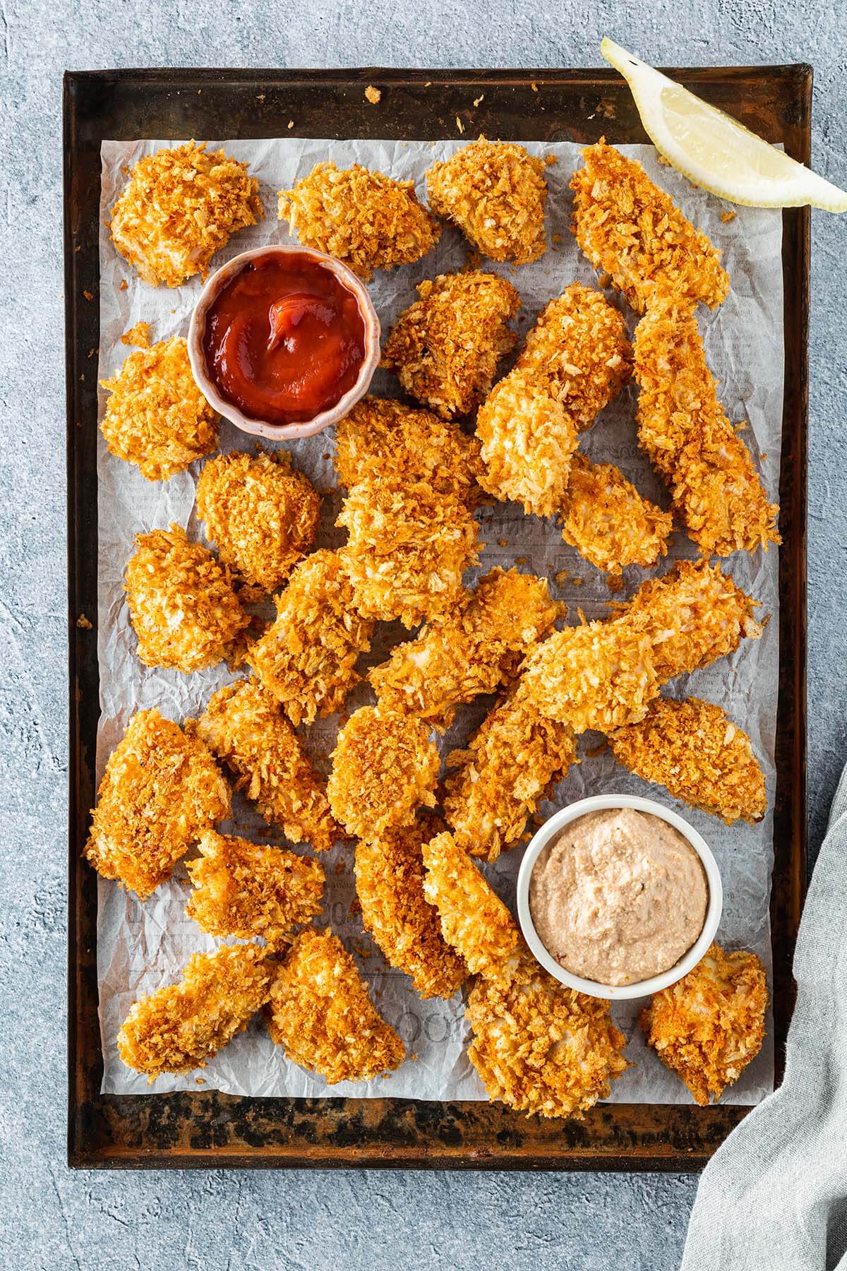 Knusprig gebackene Chicken Nuggets auf einem Blech mit zwei Dips.