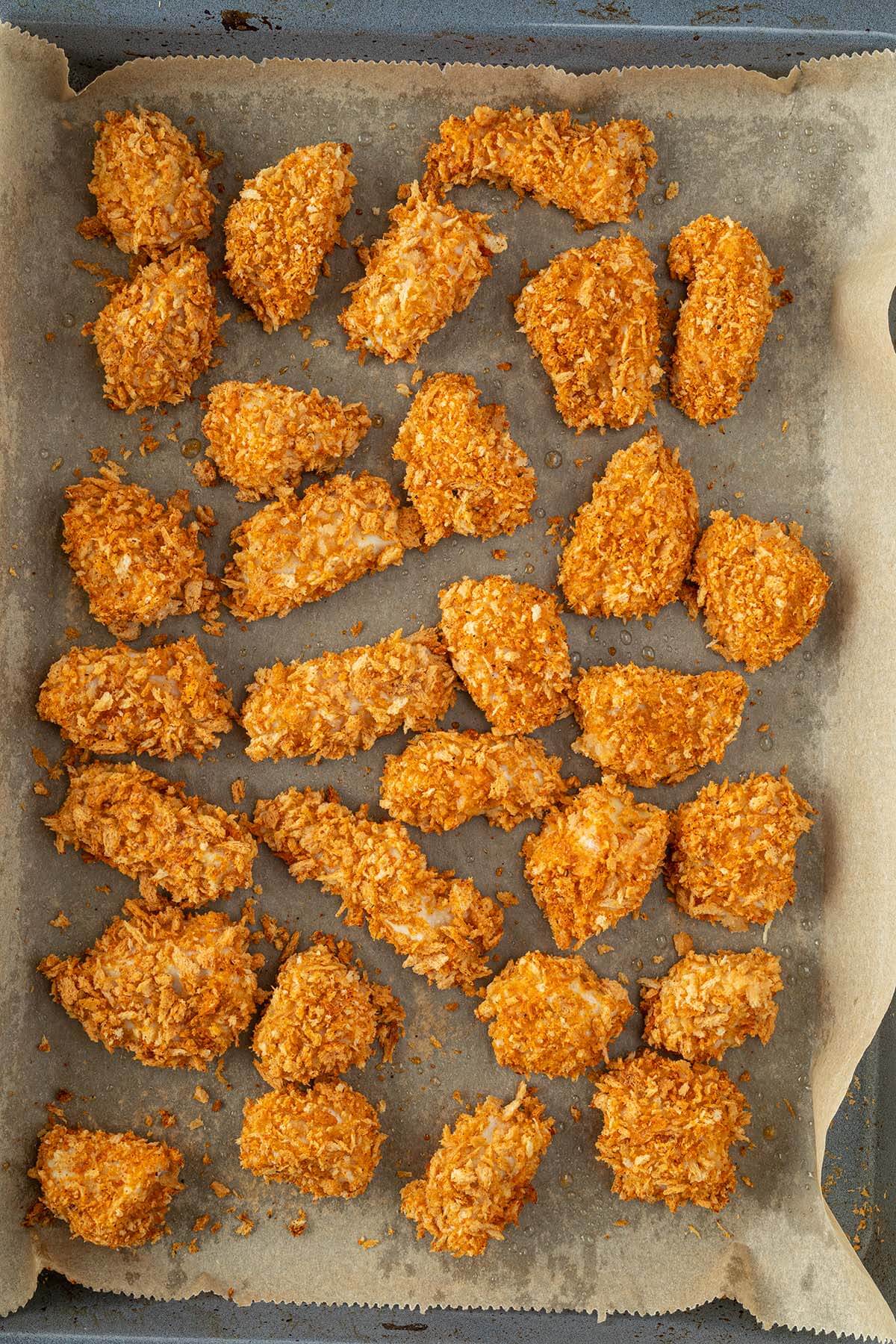 Knusprig gebackene Chicken Nuggets auf einem Blech mit Backpapier.