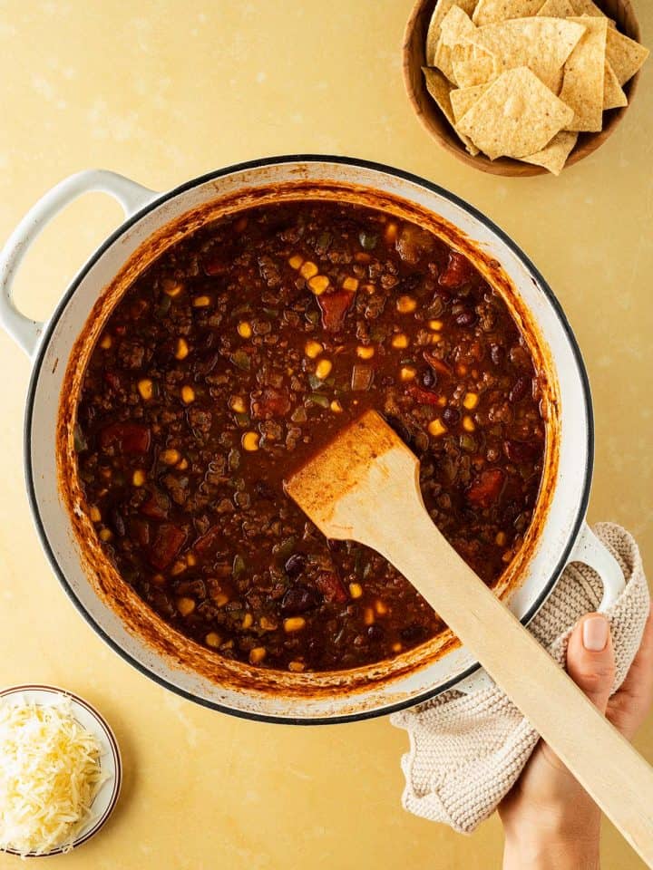 Ein Hand h&auml;lt einen gro&szlig;en Topf mit Chili con Carne, Nachos und K&auml;se im Bildrand.