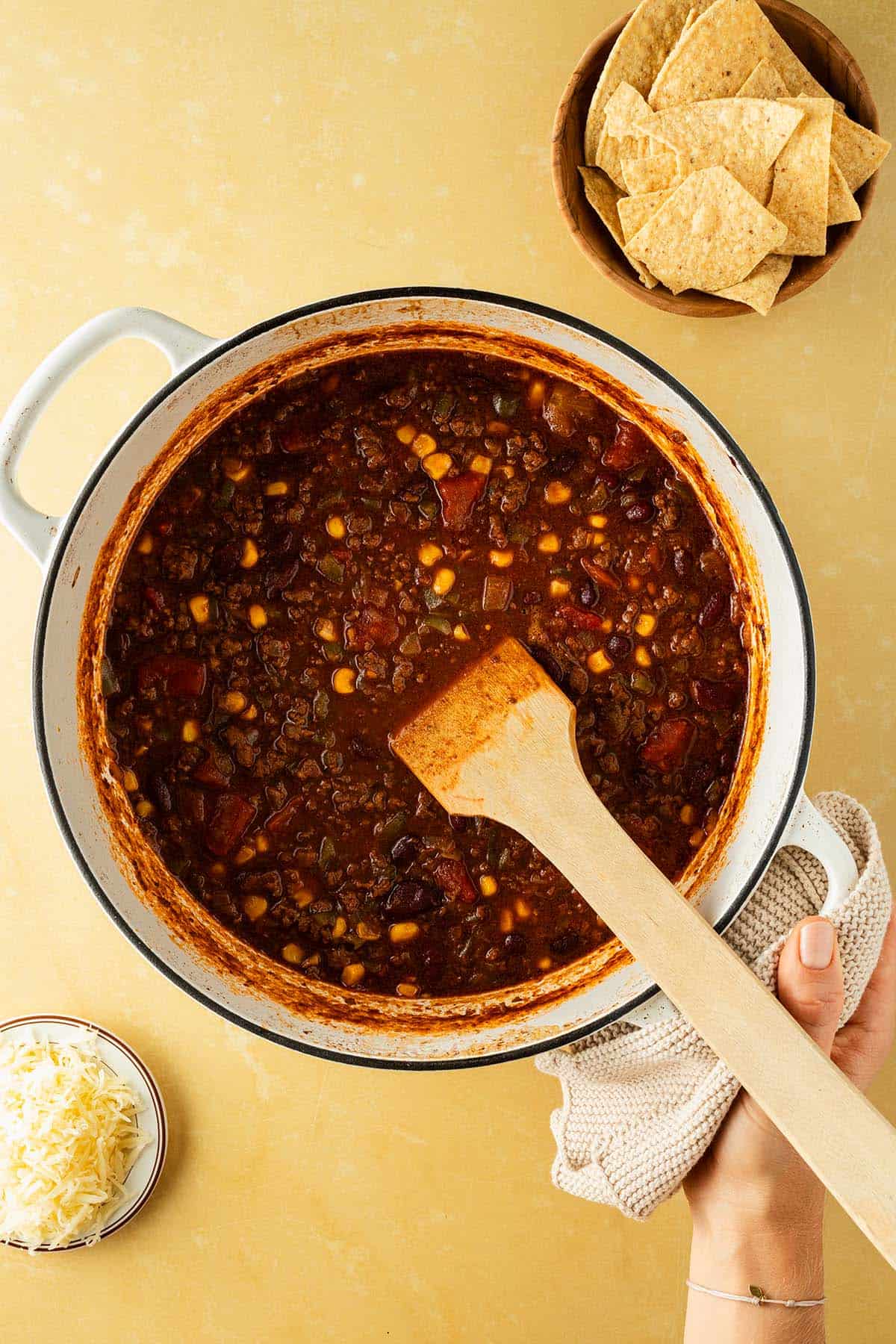Ein Hand h&auml;lt einen gro&szlig;en Topf mit Chili con Carne, Nachos und K&auml;se im Bildrand.