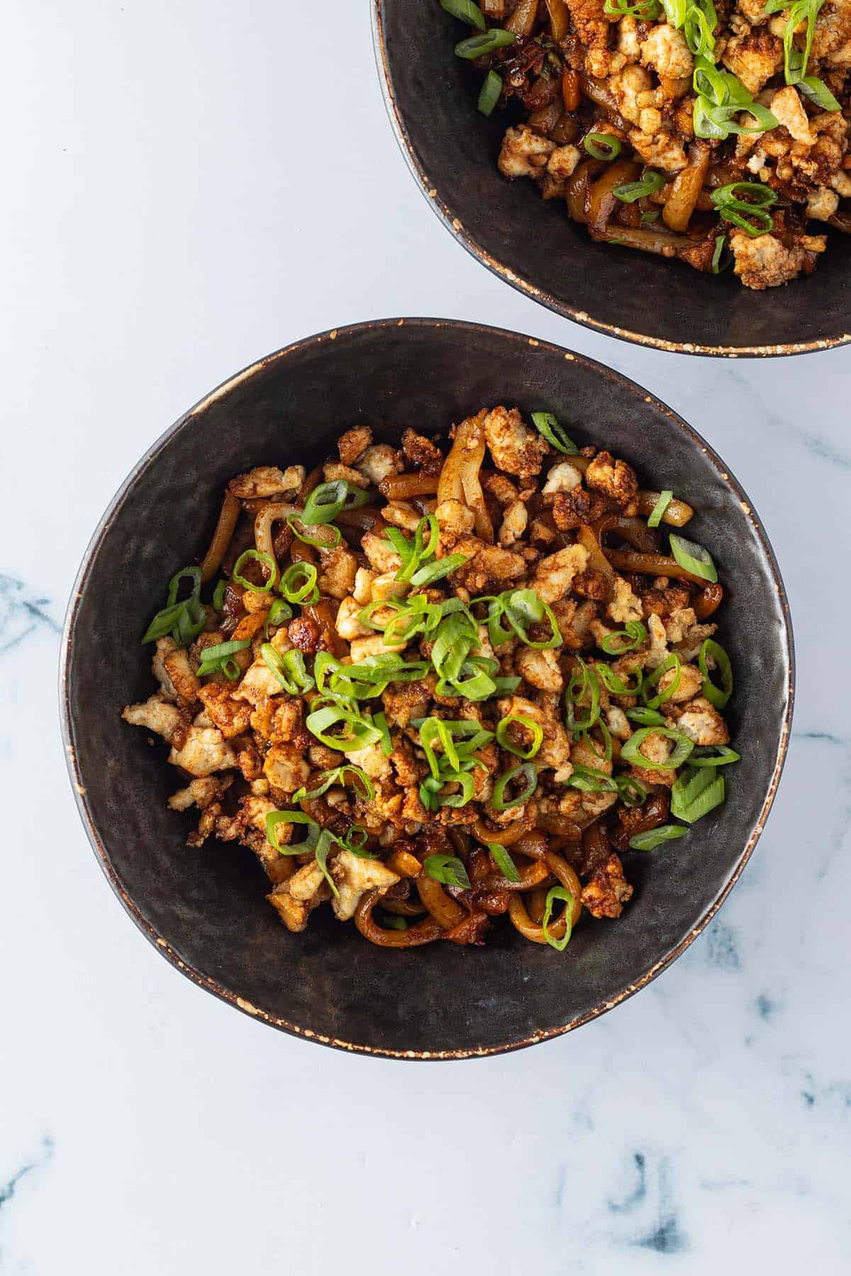 Chili Udon Nudeln auf zwei Sch&uuml;sseln verteilt, serviert mit dem knusprigen Tofu und Fr&uuml;hlingszwiebeln.