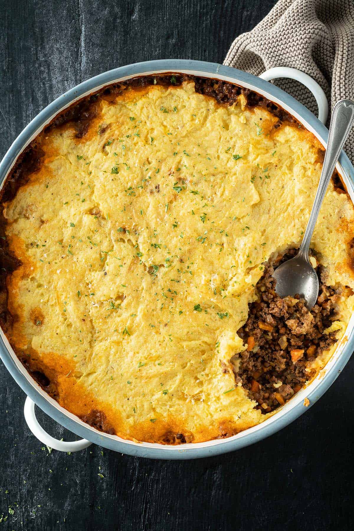 Cottage Pie in einer gro&szlig;en runden Auflaufform, wo eine Portion rausgenommen wird.