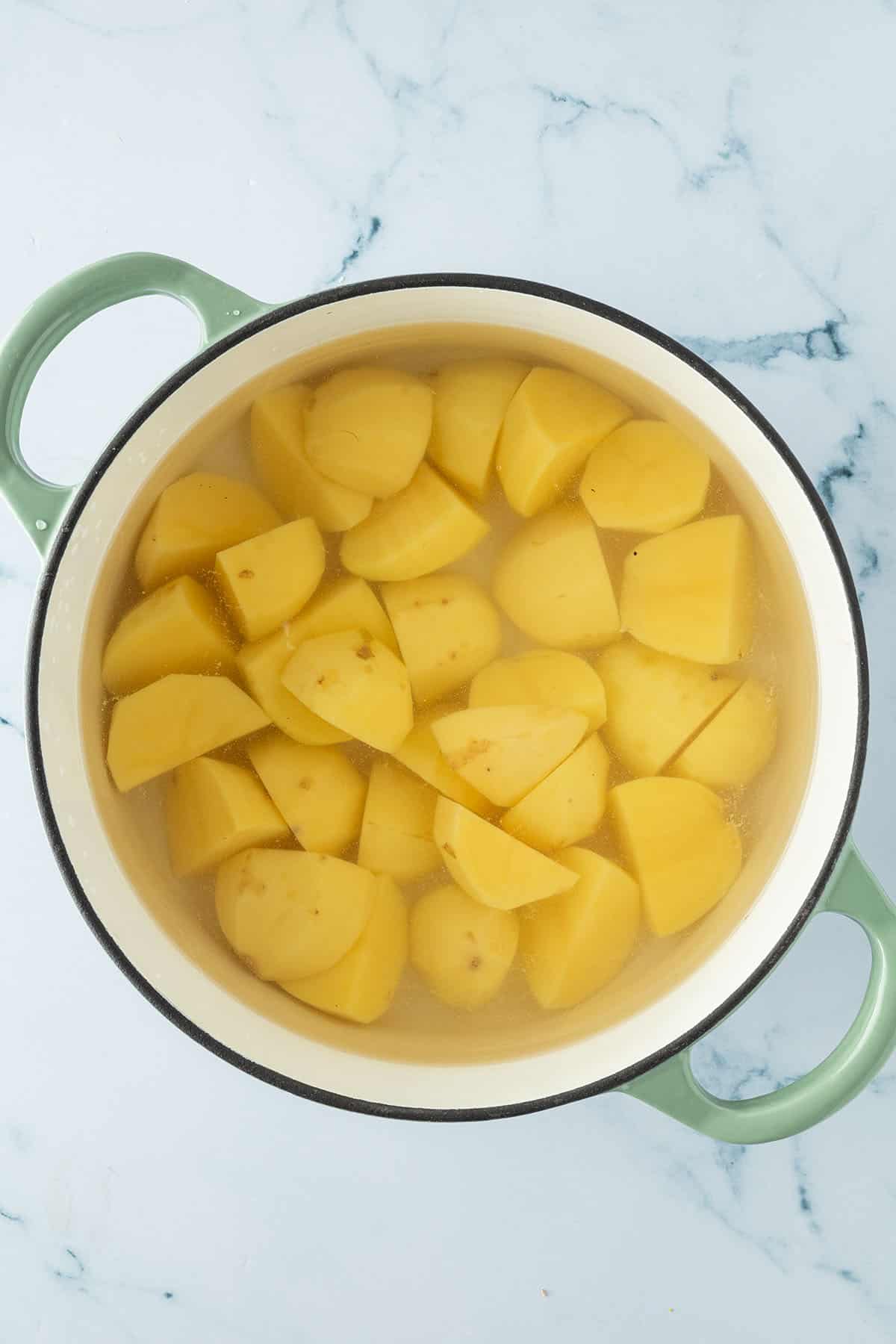 Gesch&auml;lte, grob zerkleinerte Kartoffeln in einem Topf mit Wasser.