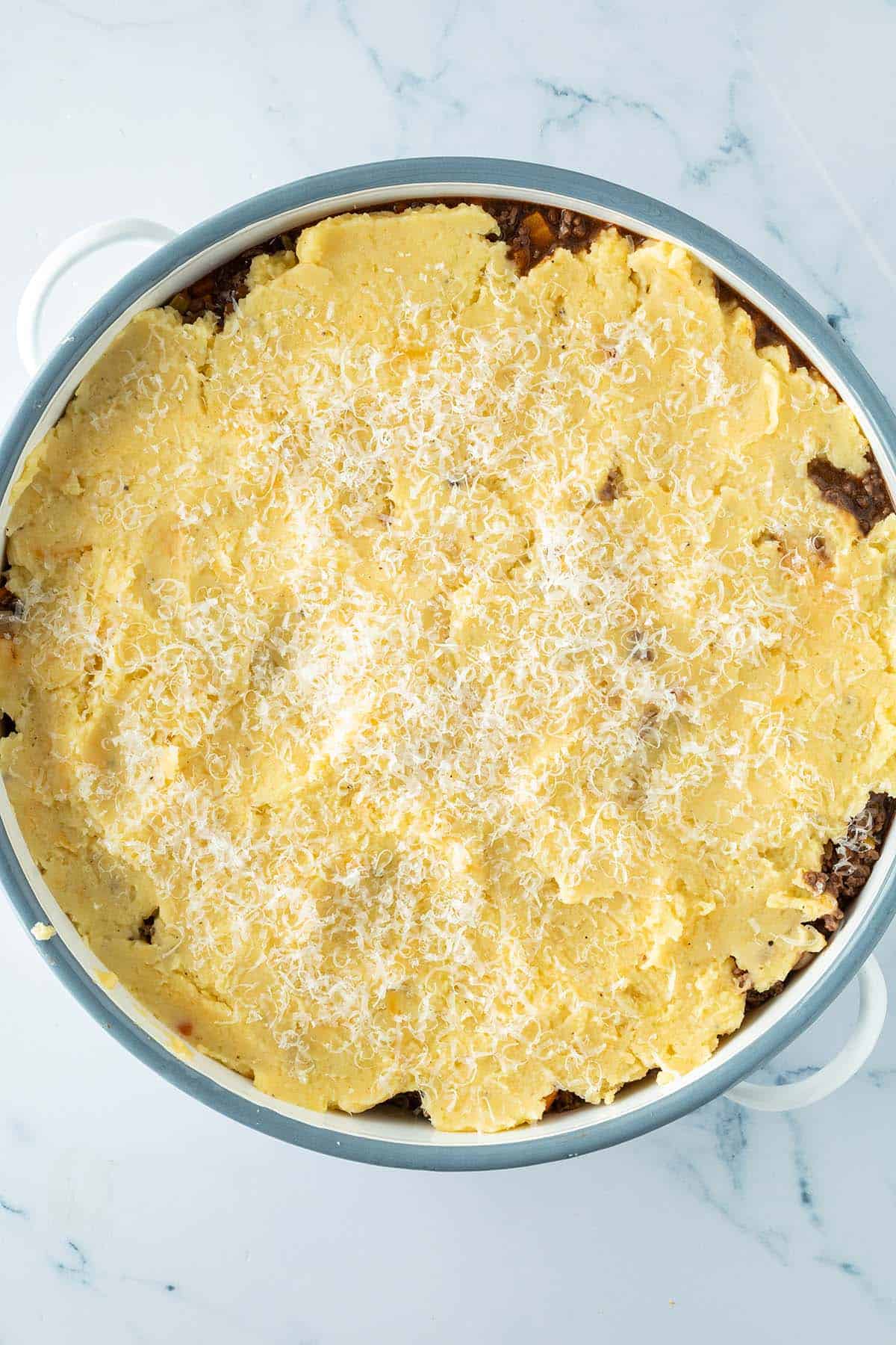Cottage Pie mit einer Hackfleischschicht und einer Schicht Kartoffelp&uuml;ree darauf in einer Auflaufform vor dem &Uuml;berbacken.