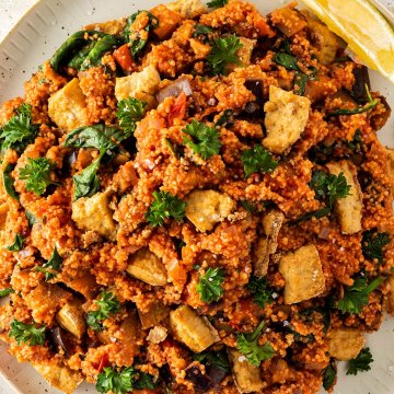 Nahaufnahme von einem Teller mit einer Couscous Gem&uuml;se Pfanne, mit frischer Petersilie und knusprigen Tofu-St&uuml;cken.