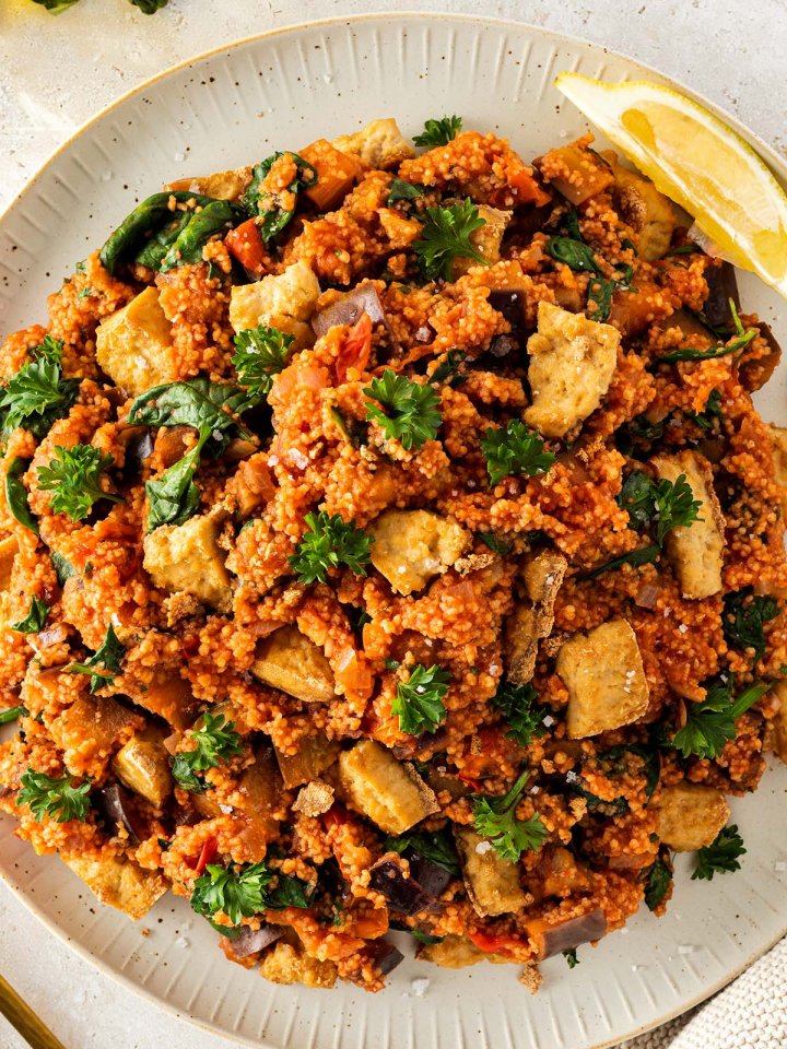 Nahaufnahme von einem Teller mit einer Couscous Gemüse Pfanne, mit frischer Petersilie und knusprigen Tofu-Stücken.