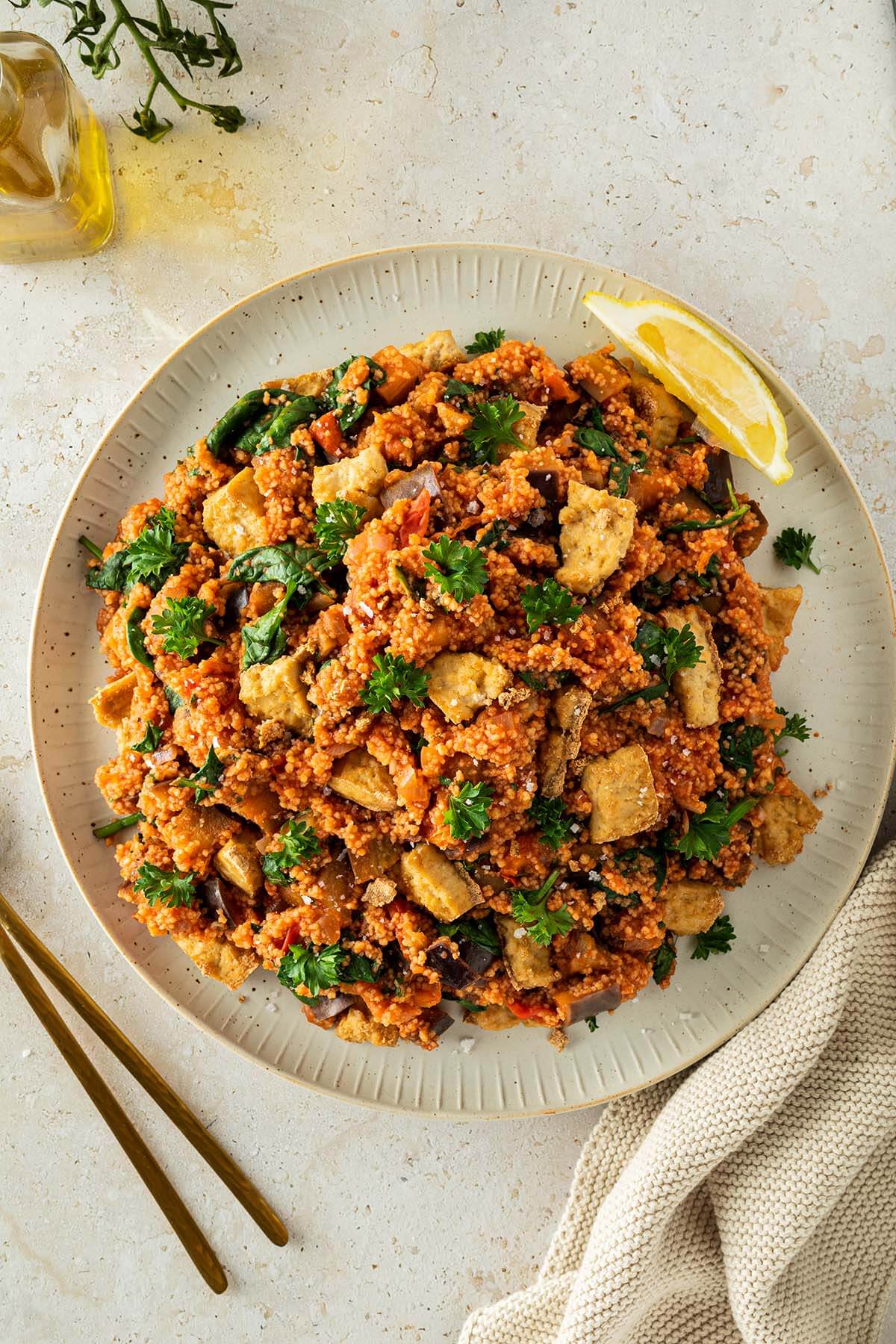 Couscous-Gem&uuml;se-Pfanne serviert auf einem beigen Teller mit frischer Petersilie und knusprigen Tofust&uuml;ckchen. Deko im Bildrand.