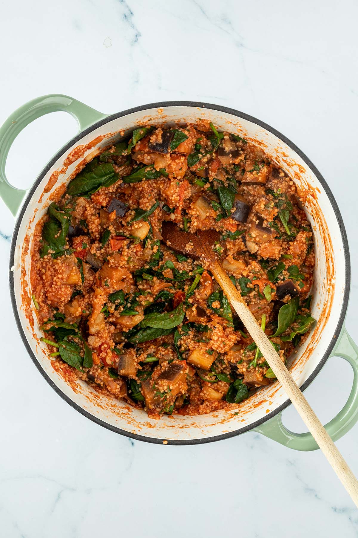 Vogelperspektive auf einen Topf mit einer Couscous Gem&uuml;se Pfanne mit frischem Spinat und Tomatensauce.