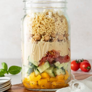 Couscous Salat in einem gro&szlig;en Glas vor einem beigen Hintergrund mit Deko im Bildrand.
