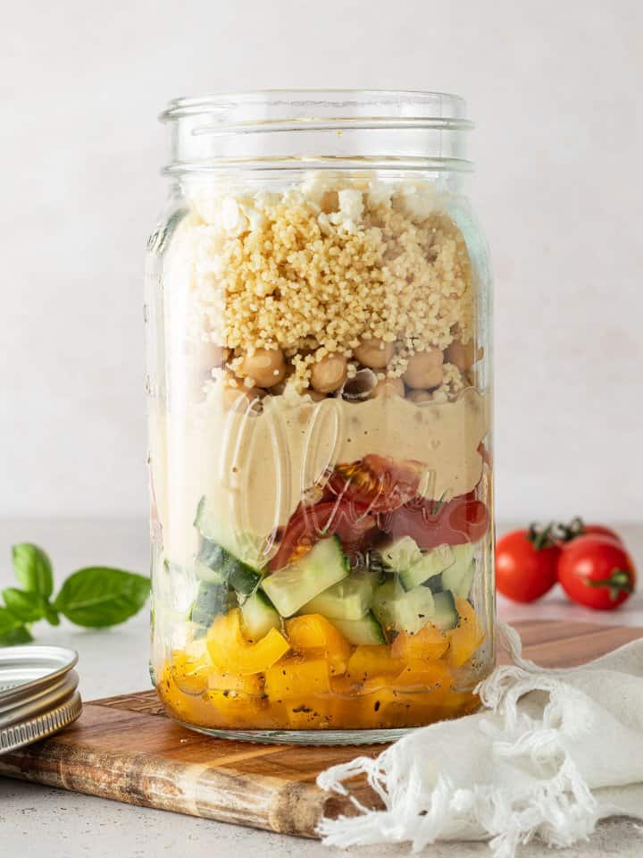 Couscous Salat in einem gro&szlig;en Glas vor einem beigen Hintergrund mit Deko im Bildrand.