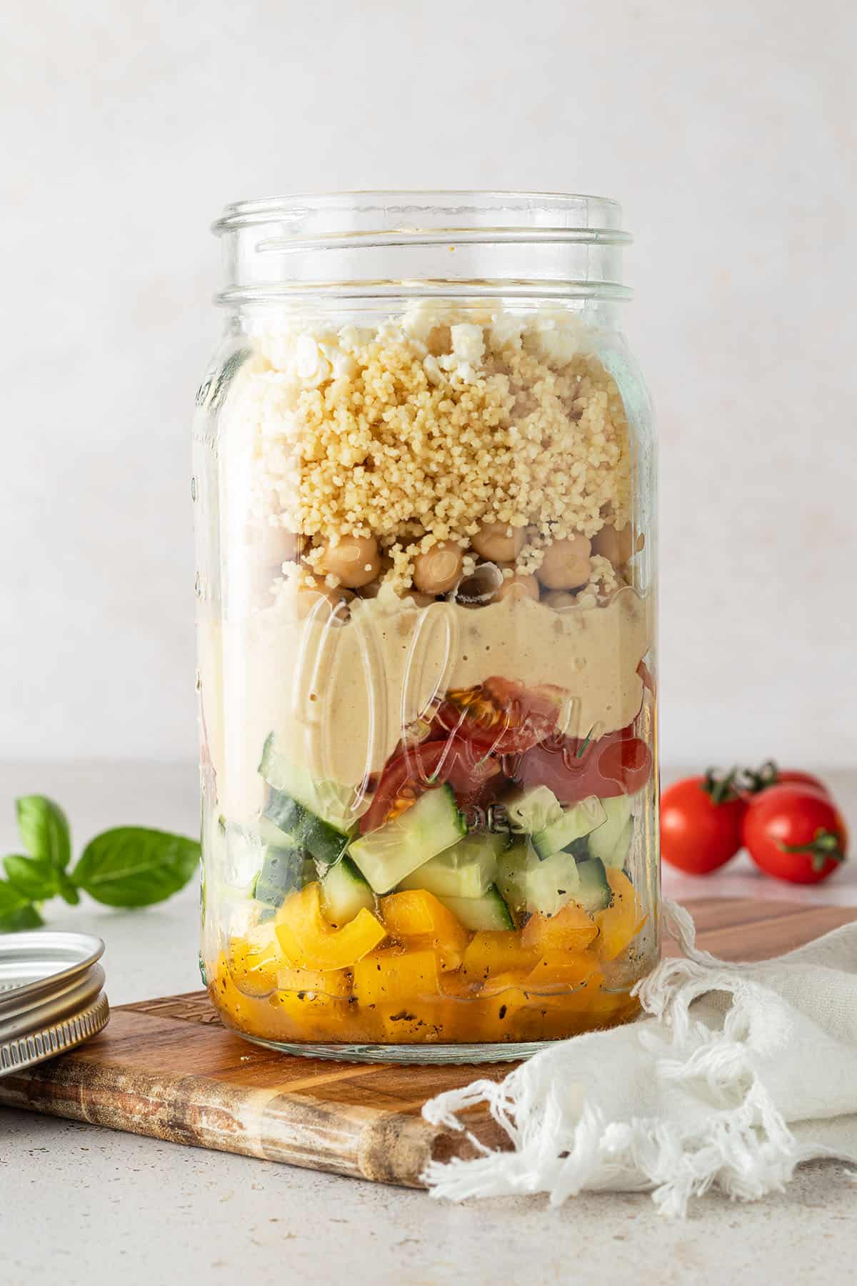 Couscous Salat in einem gro&szlig;en Glas vor einem beigen Hintergrund mit Deko im Bildrand.