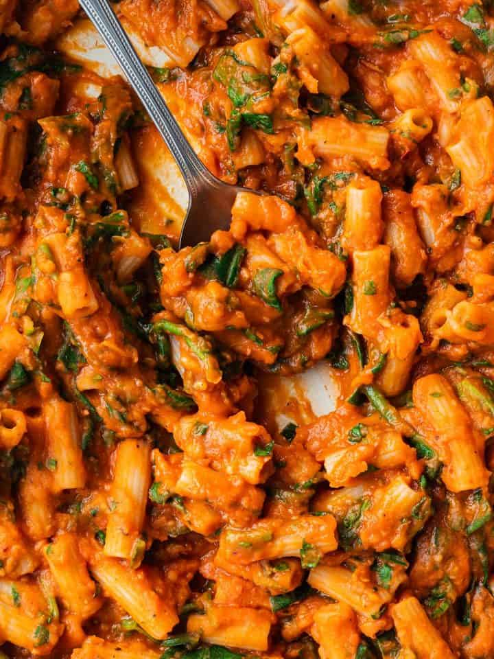 Ein L&ouml;ffel f&auml;hrt durch eine Pfanne mit Nudeln in einer cremigen Tomatensauce.
