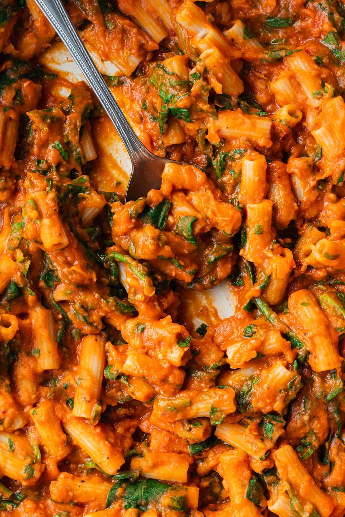 Ein L&ouml;ffel f&auml;hrt durch eine Pfanne mit Nudeln in einer cremigen Tomatensauce.