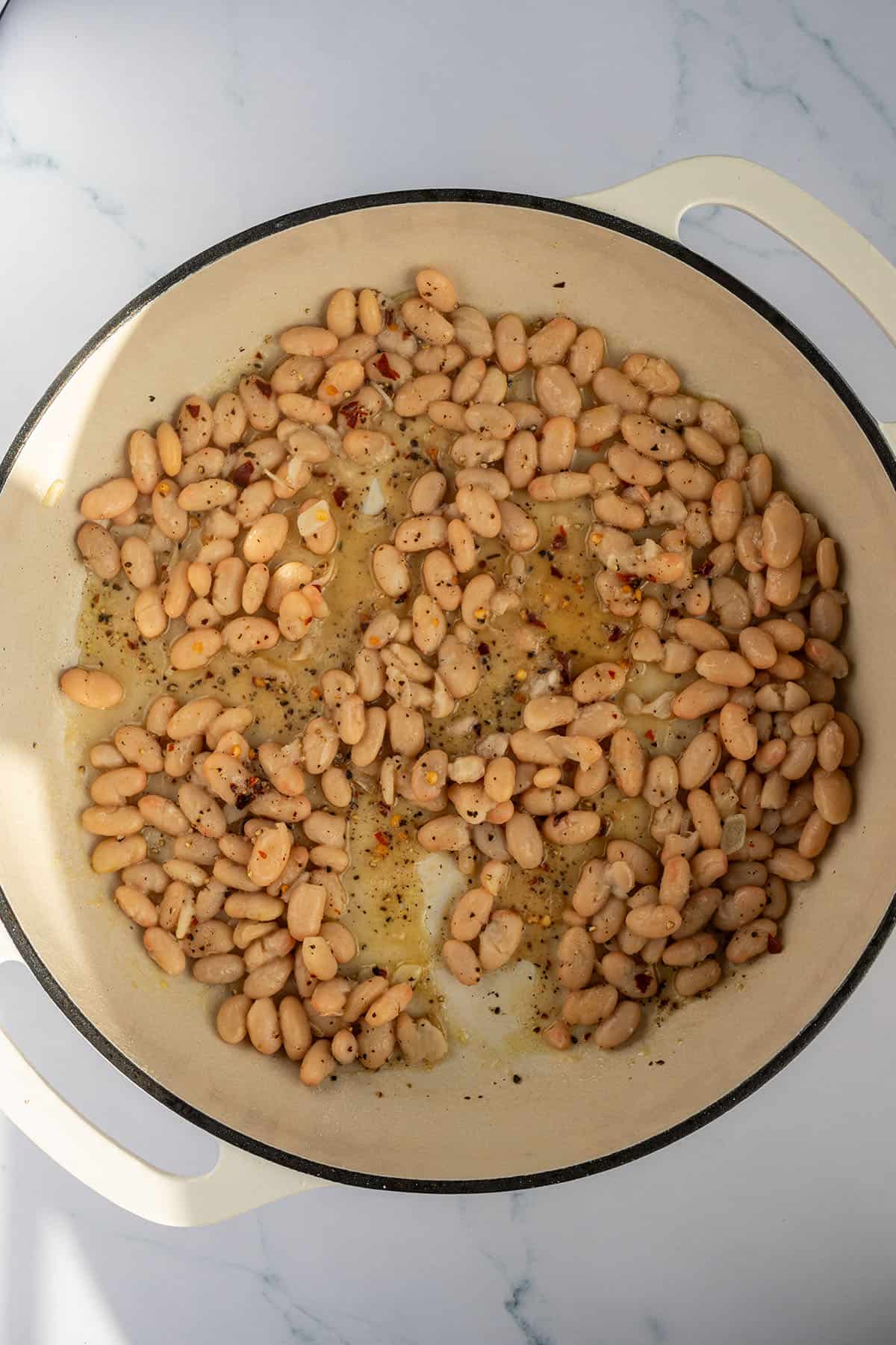 Wei&szlig;e Bohnen und Knoblauch in einer Pfanne.
