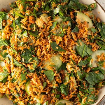 Knuspriger Reissalat mit Gurke, Spinat, Kr&auml;utern und Erdnussdressing auf einem gro&szlig;en Teller.