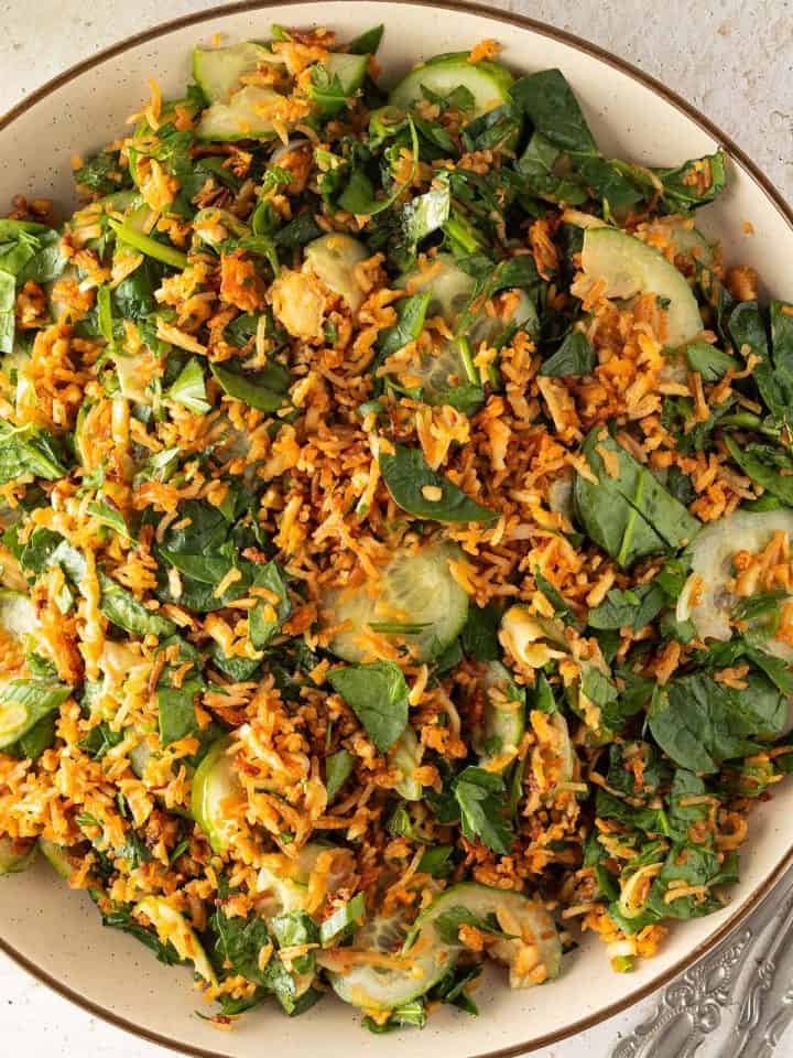 Knuspriger Reissalat mit Gurke, Spinat, Kr&auml;utern und Erdnussdressing auf einem gro&szlig;en Teller.
