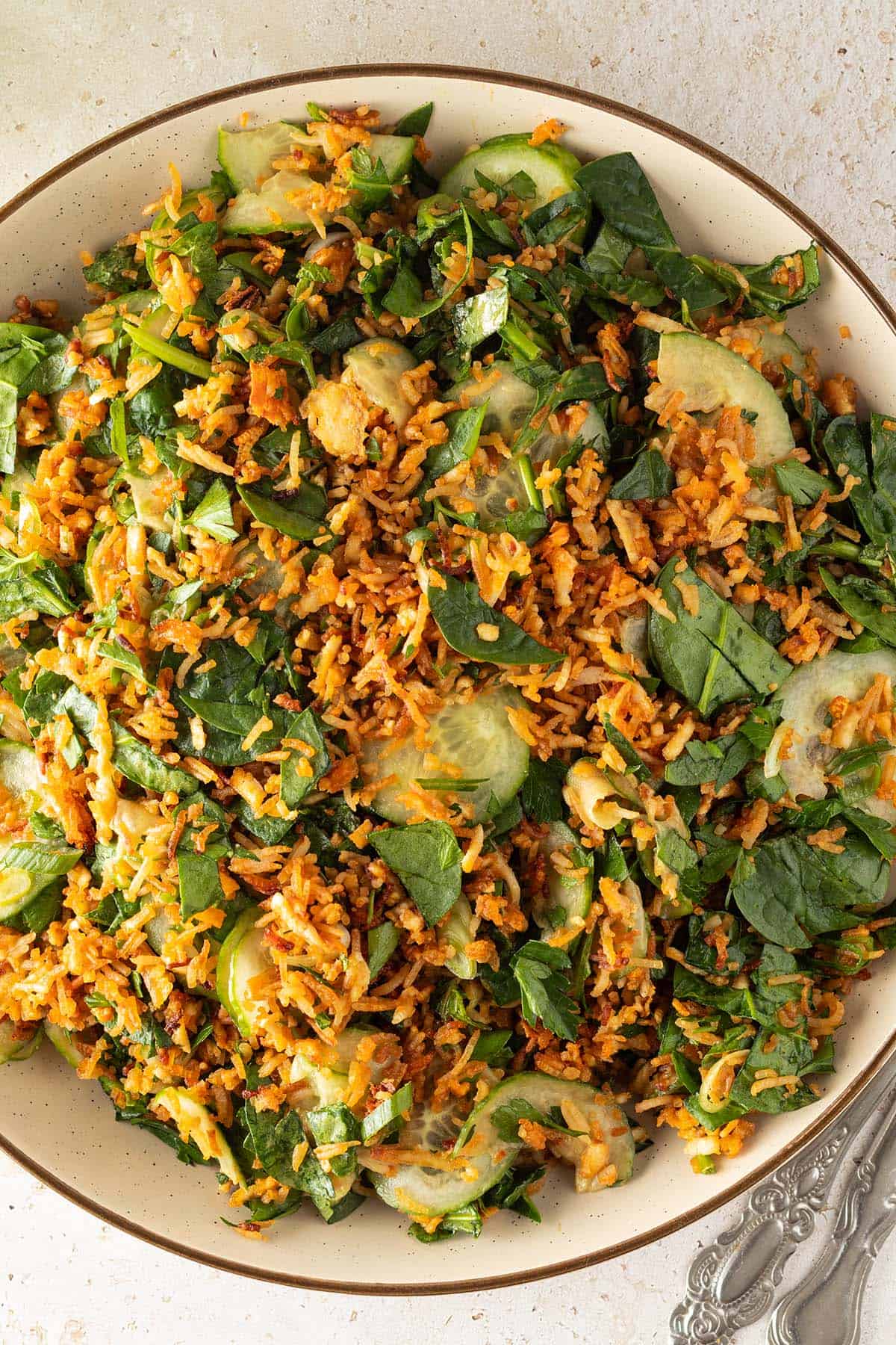 Knuspriger Reissalat mit Gurke, Spinat, Kr&auml;utern und Erdnussdressing auf einem gro&szlig;en Teller.
