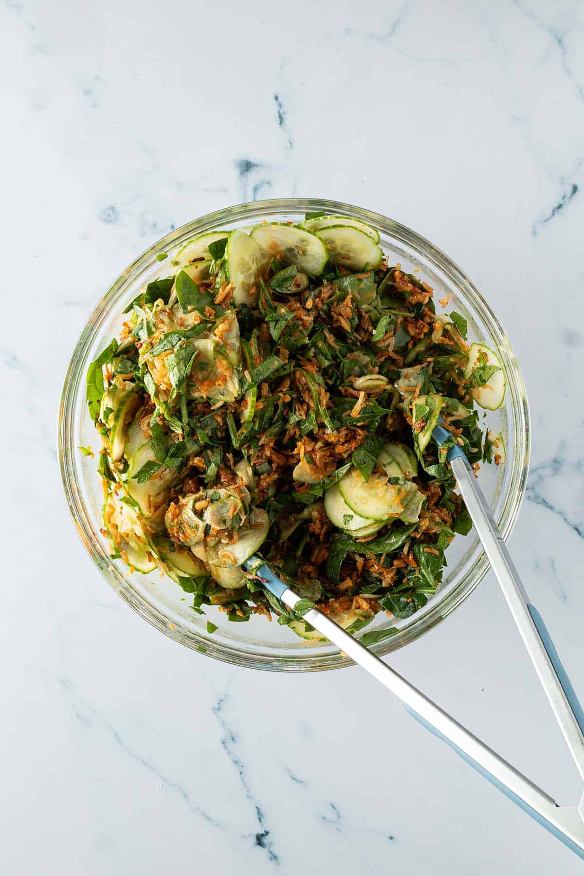 Gem&uuml;se, knuspriger Reis, Tofu und Dressing werden in einer gro&szlig;en Sch&uuml;ssel mit einer K&uuml;chenzange vermischt.