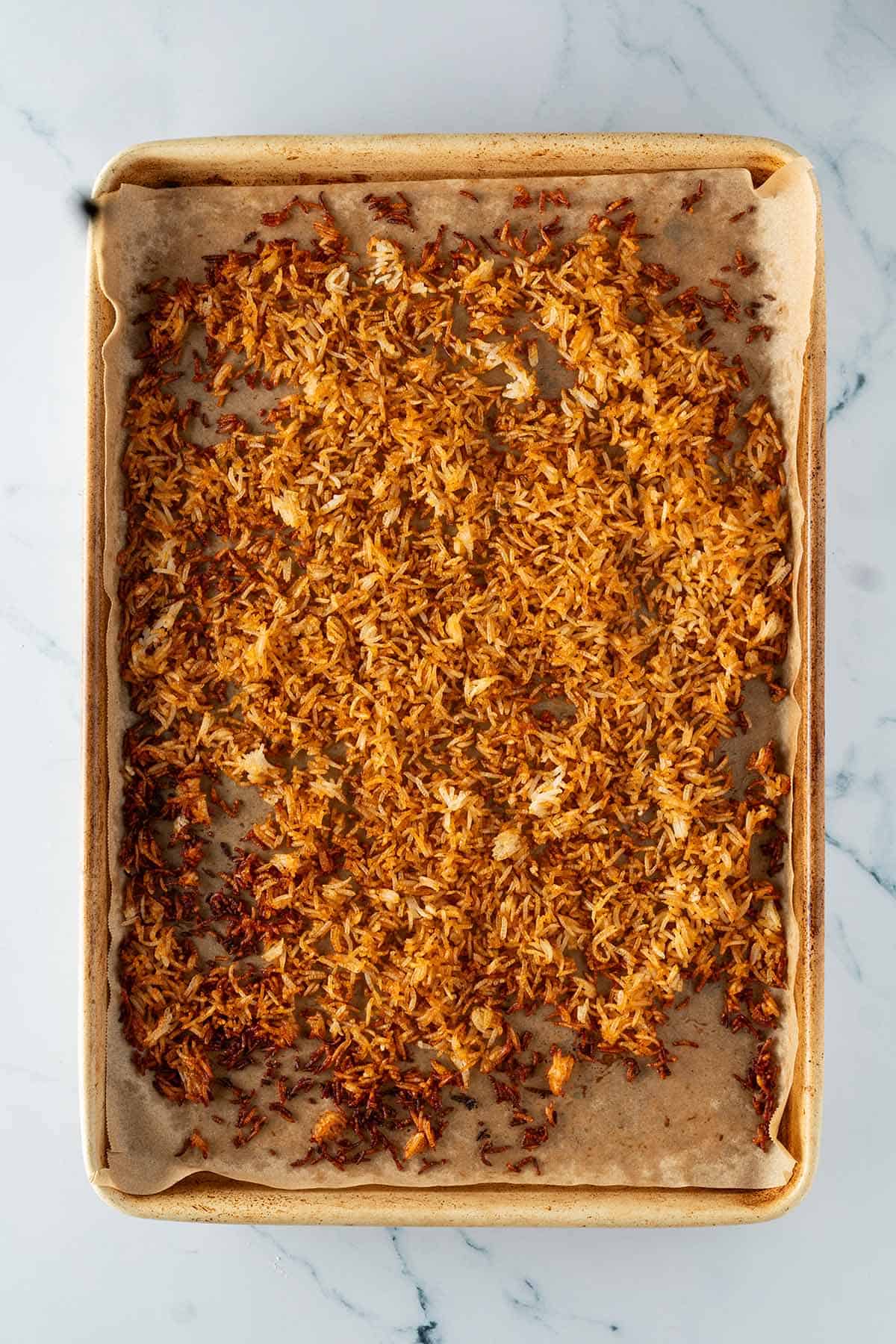 Knusprig, braun ger&ouml;steter Reis auf einem mit Backpapier ausgelegten Blech.