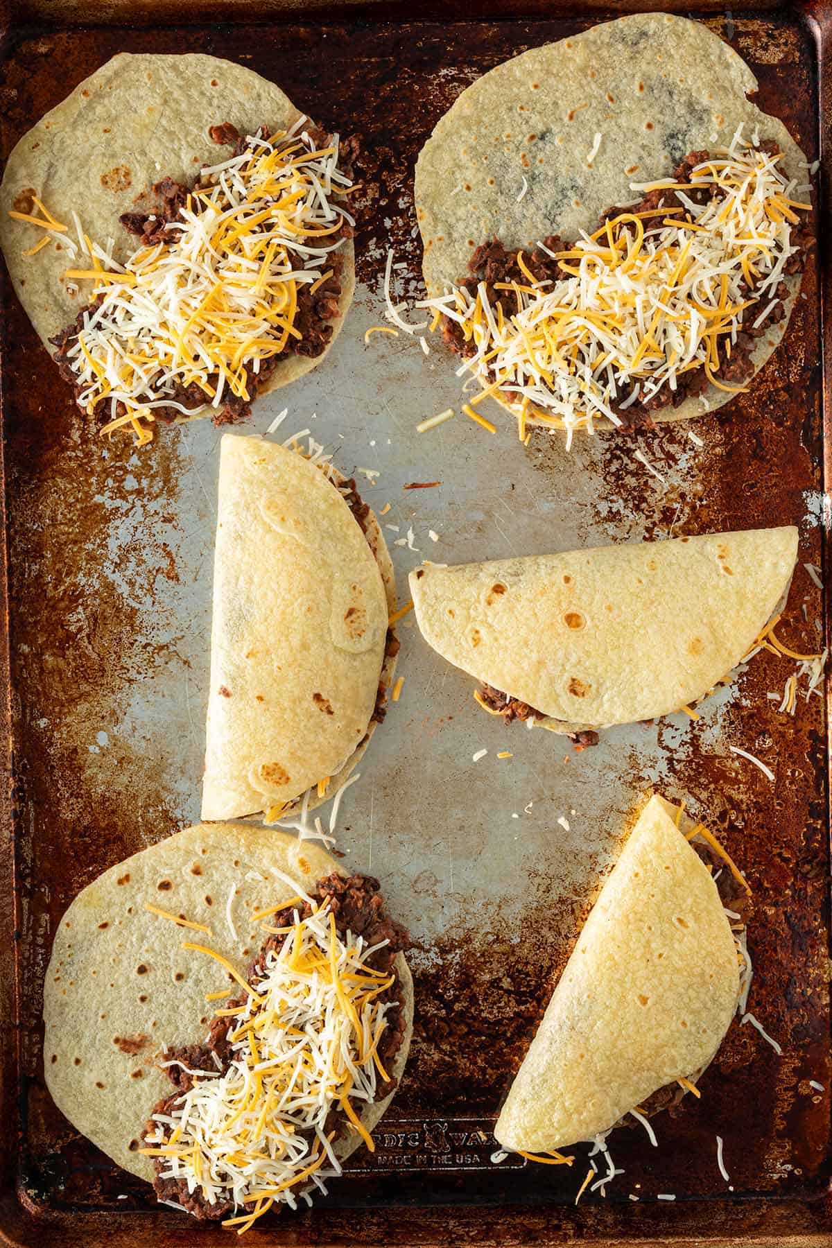 Tortillas mit schwarzer Bohnenf&uuml;llung und K&auml;se gef&uuml;llt und teilweise zusammengeklappt auf einem Blech.