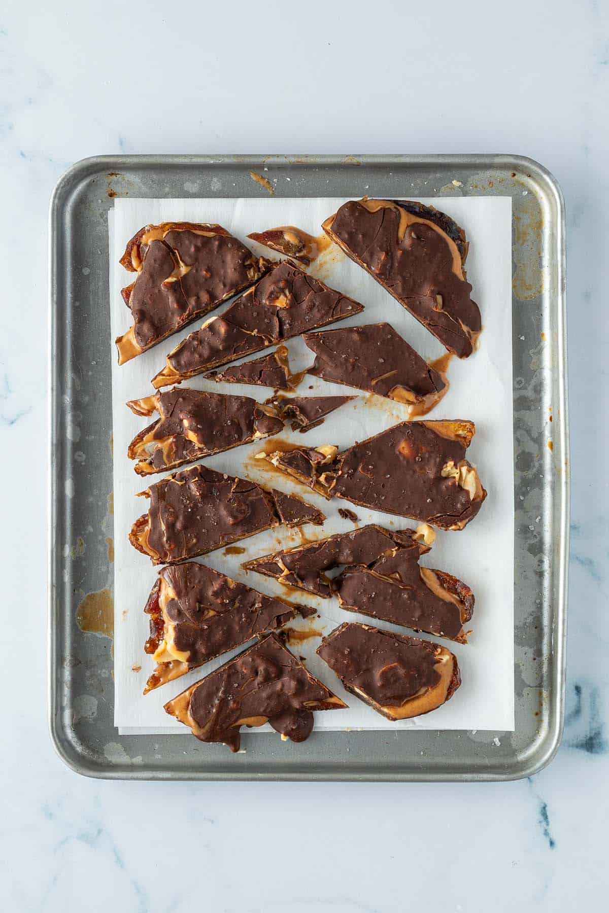Ind St&uuml;cke geschnittene Datteln mit Schokolade und Erdnussbutter auf einem kleinen Blech mit Butterpapier.
