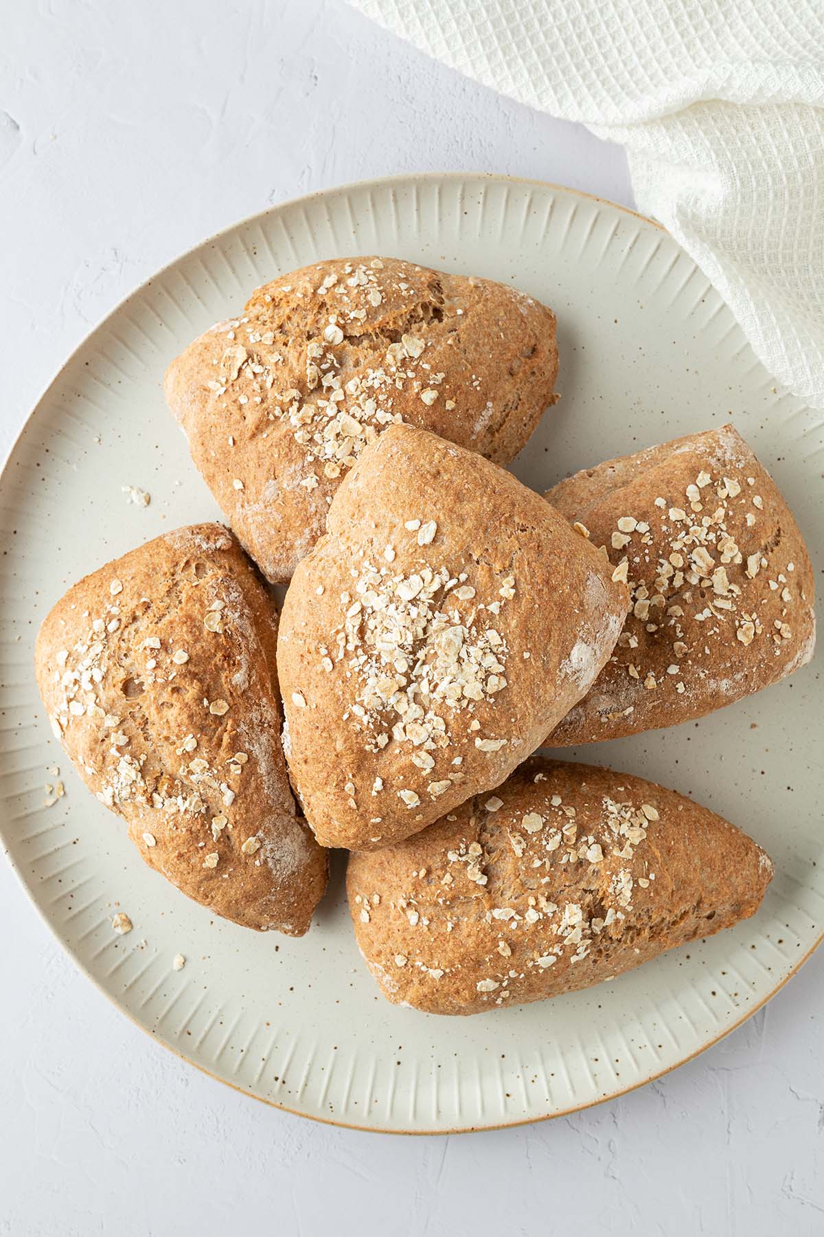 Ein Teller mit fünf Dinkelvollkornbrötchen auf einem weißen Untergrund.