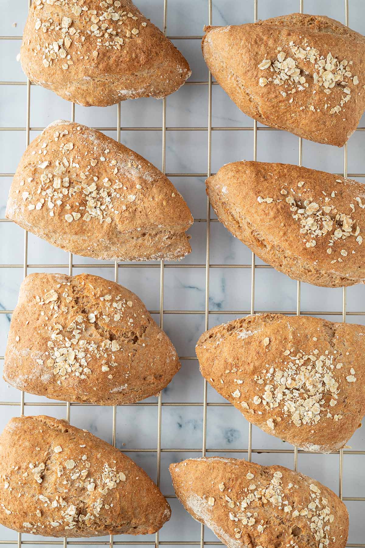 Acht knusprig gebackene Vollkornbrötchen auf einem Abkühlgitter.