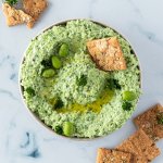 Edamame Dip in einer Sch&uuml;ssel, serviert mit Crackern und frischer Petersilie.