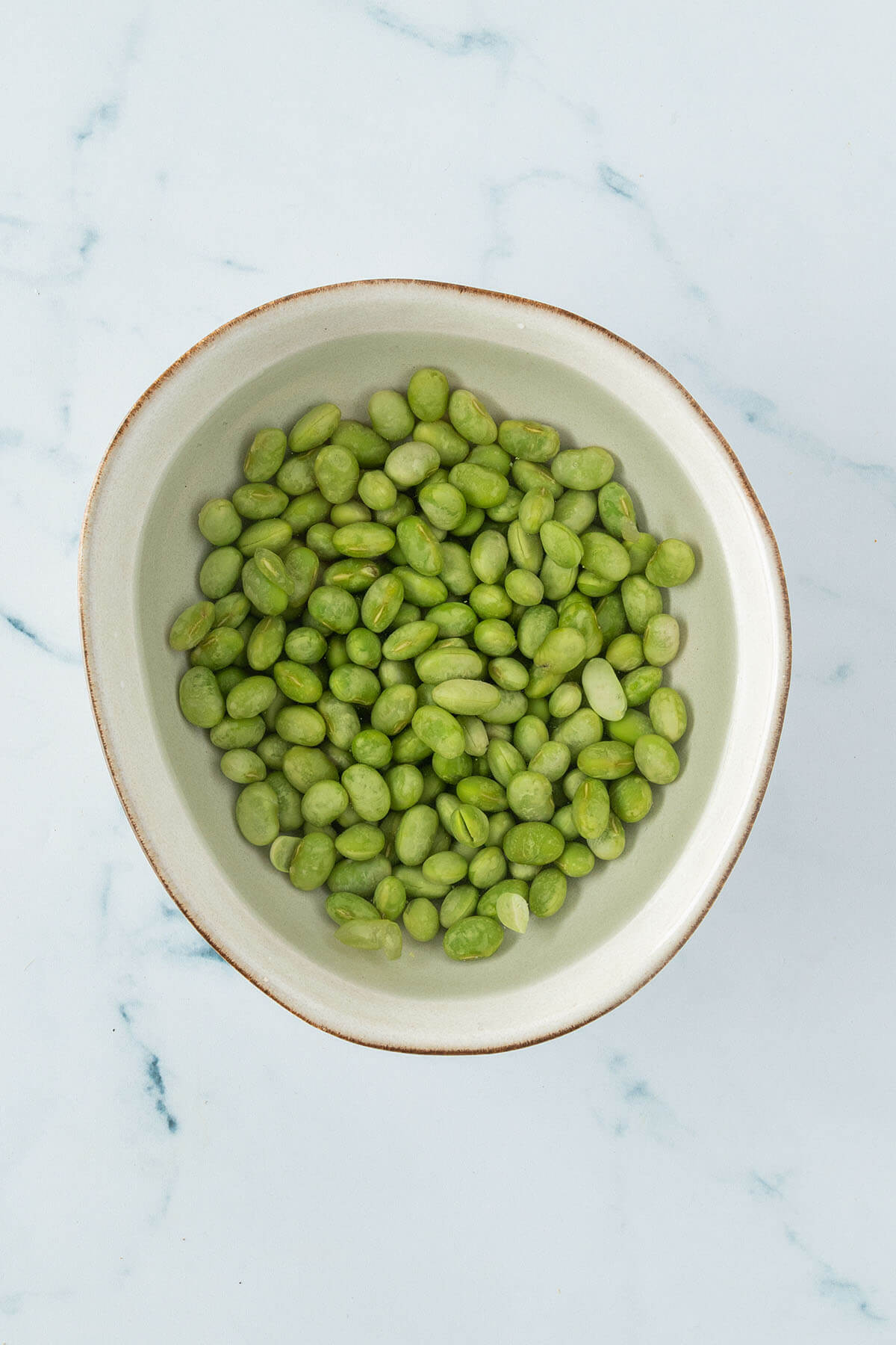 Vogelperspektive auf eine Sch&uuml;ssel mit Edamame Bohnen, die in warmen Wasser auftauen.