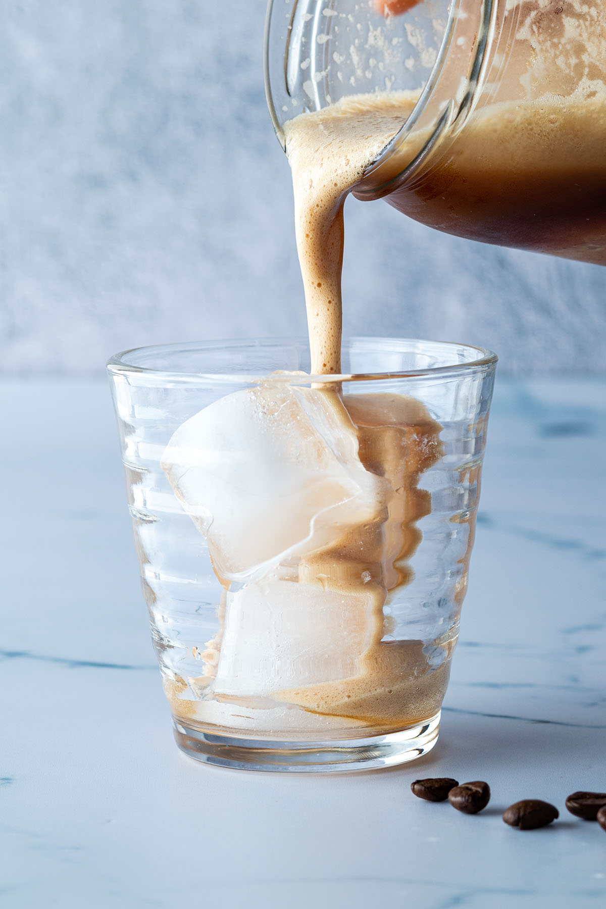 Eiskaffee wird in eine Glas mit Eisw&uuml;rfeln gegossen.
