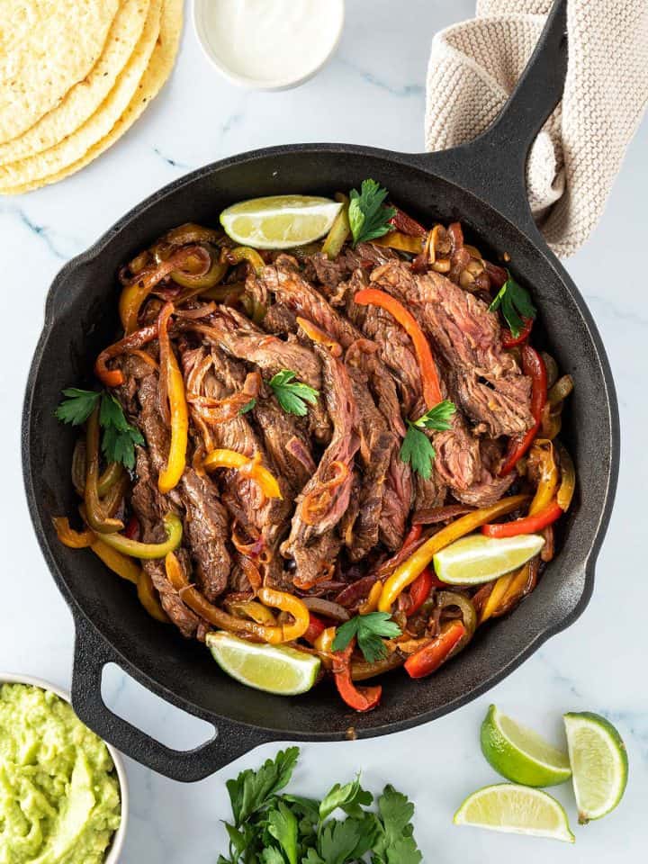 Fajitas Pfanne mit Rindfleisch serviert mit Tortillas, Sourcoream, Guacamole und Limette.
