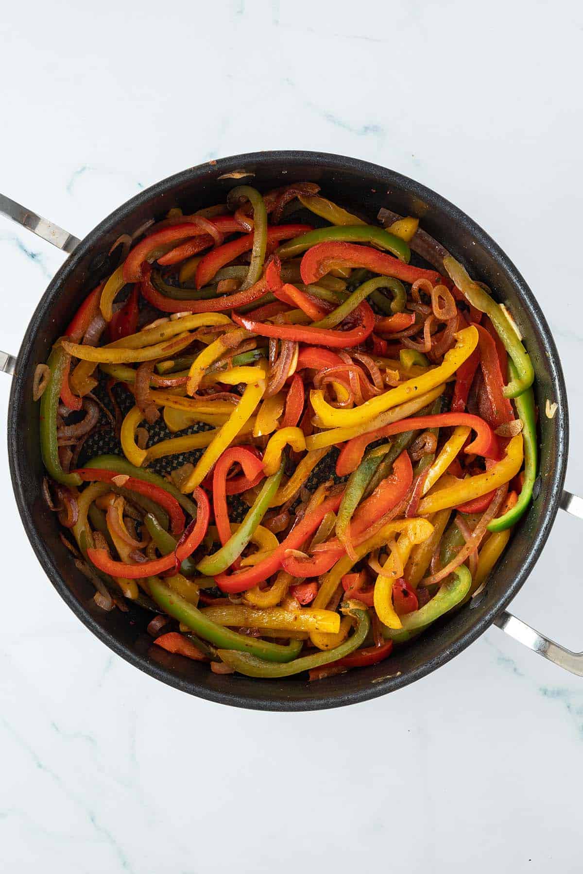 Weich angebratene Paprika- und Zwiebelstreifen in einer gro&szlig;en Pfanne.