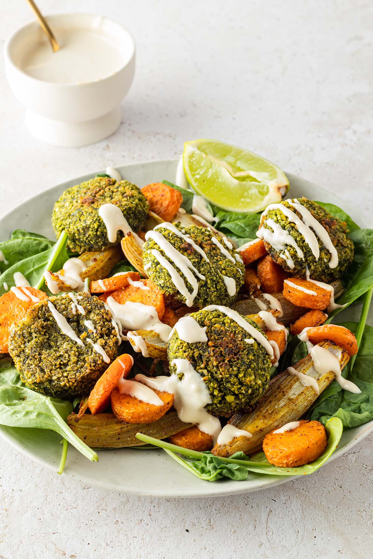 Orientalische Falafel Bowl mit Tahini Dressing auf einem Teller, im Hintergrund eine Schüssel mit dem Dressing.
