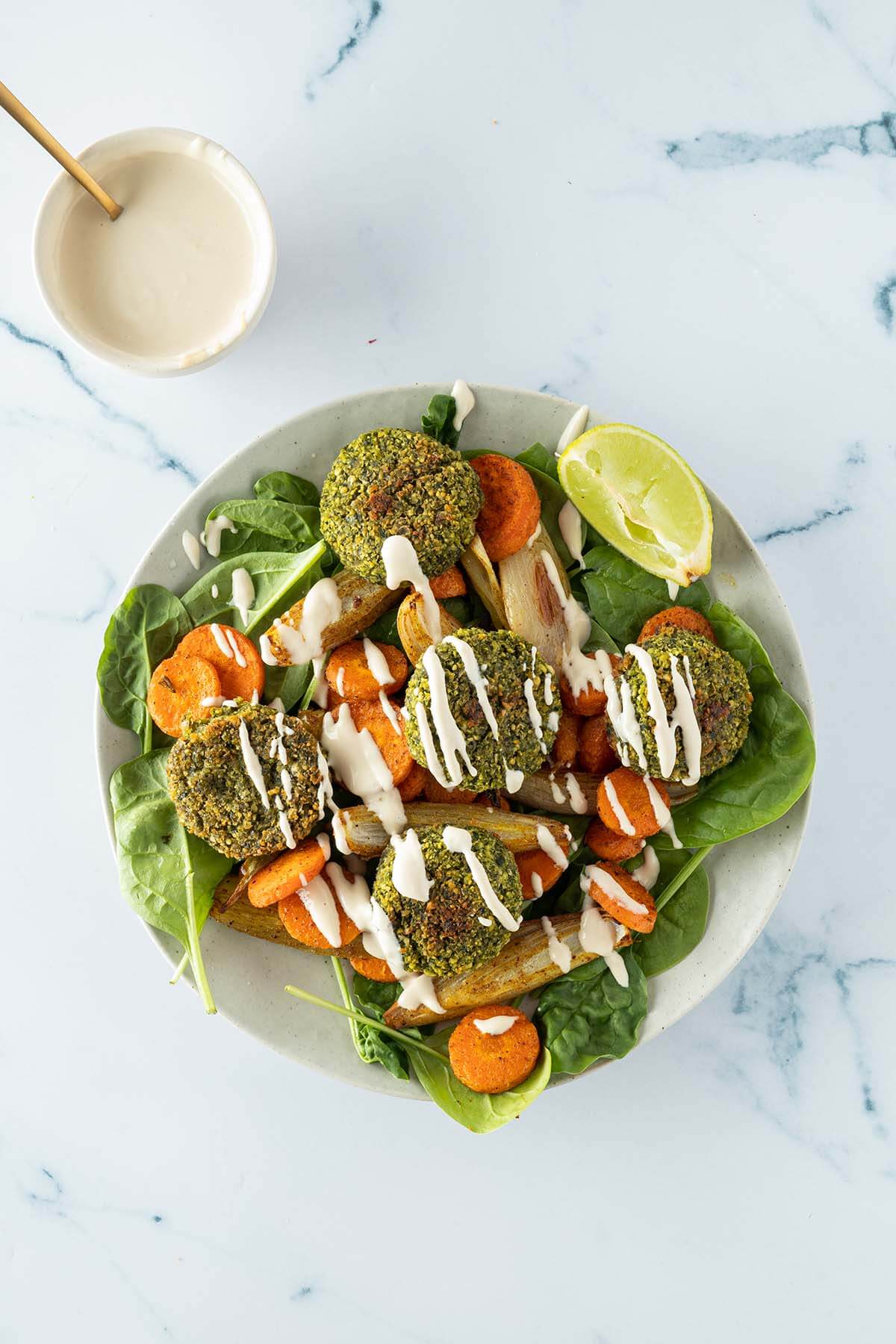 Fertige Falafel Bowl mit Tahini Dressing auf einem Marmor-Untergrund.