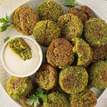 Im Ofen knusprig gebackene Falafel auf einem Teller mit einem cremigen Tahini-Dip, Deko im Bildrand.