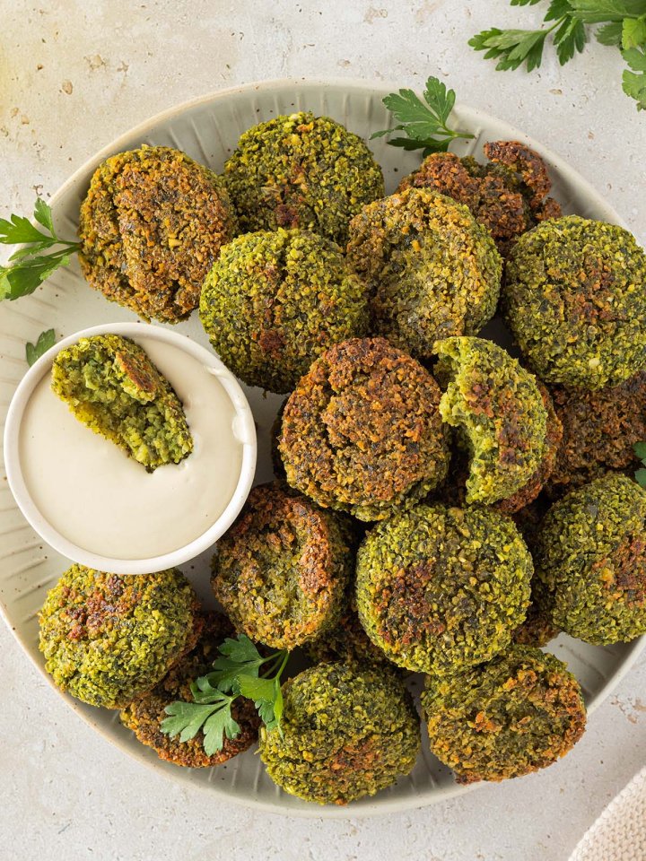 Im Ofen knusprig gebackene Falafel auf einem Teller mit einem cremigen Tahini-Dip, Deko im Bildrand.