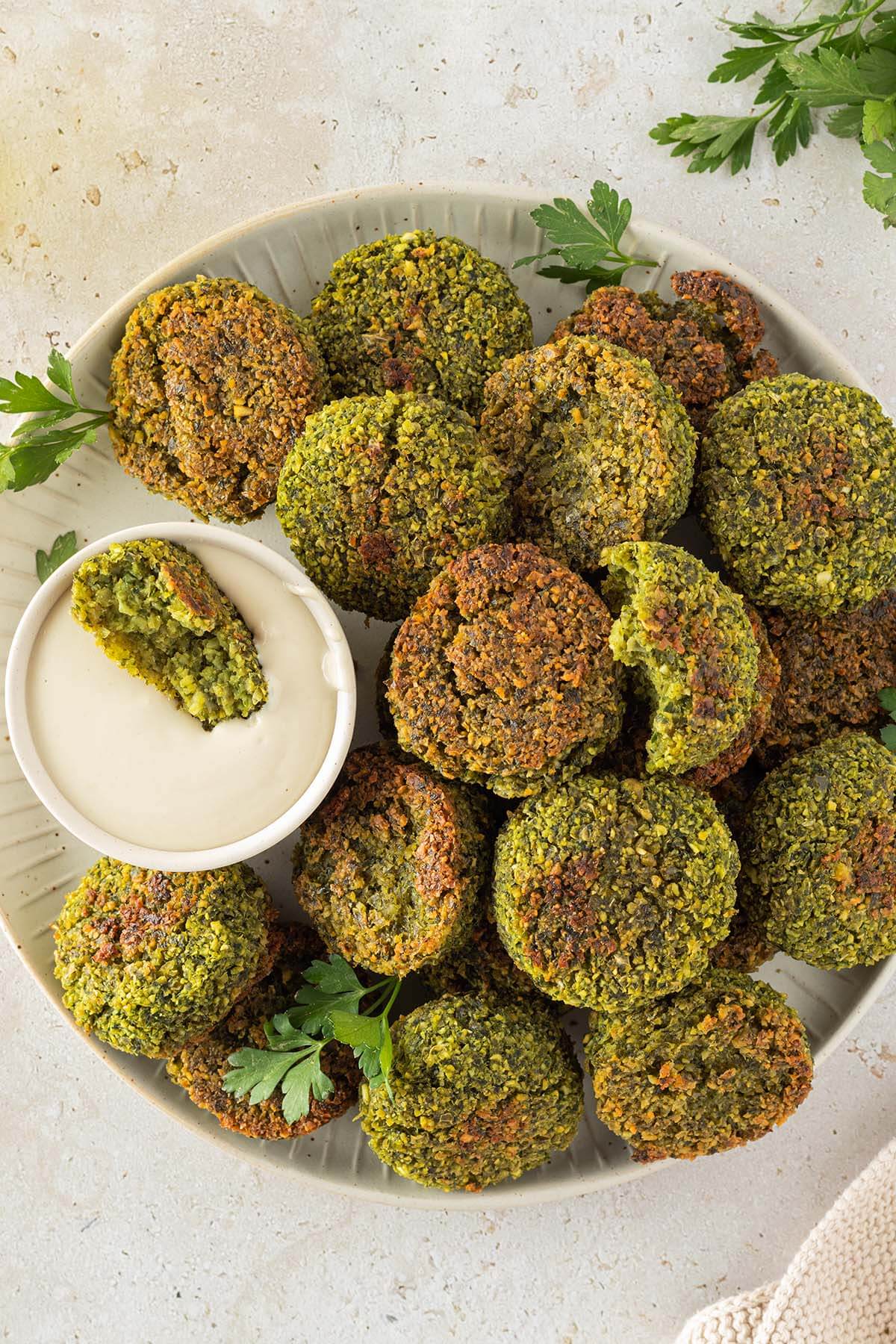 Im Ofen knusprig gebackene Falafel auf einem Teller mit einem cremigen Tahini-Dip, Deko im Bildrand.