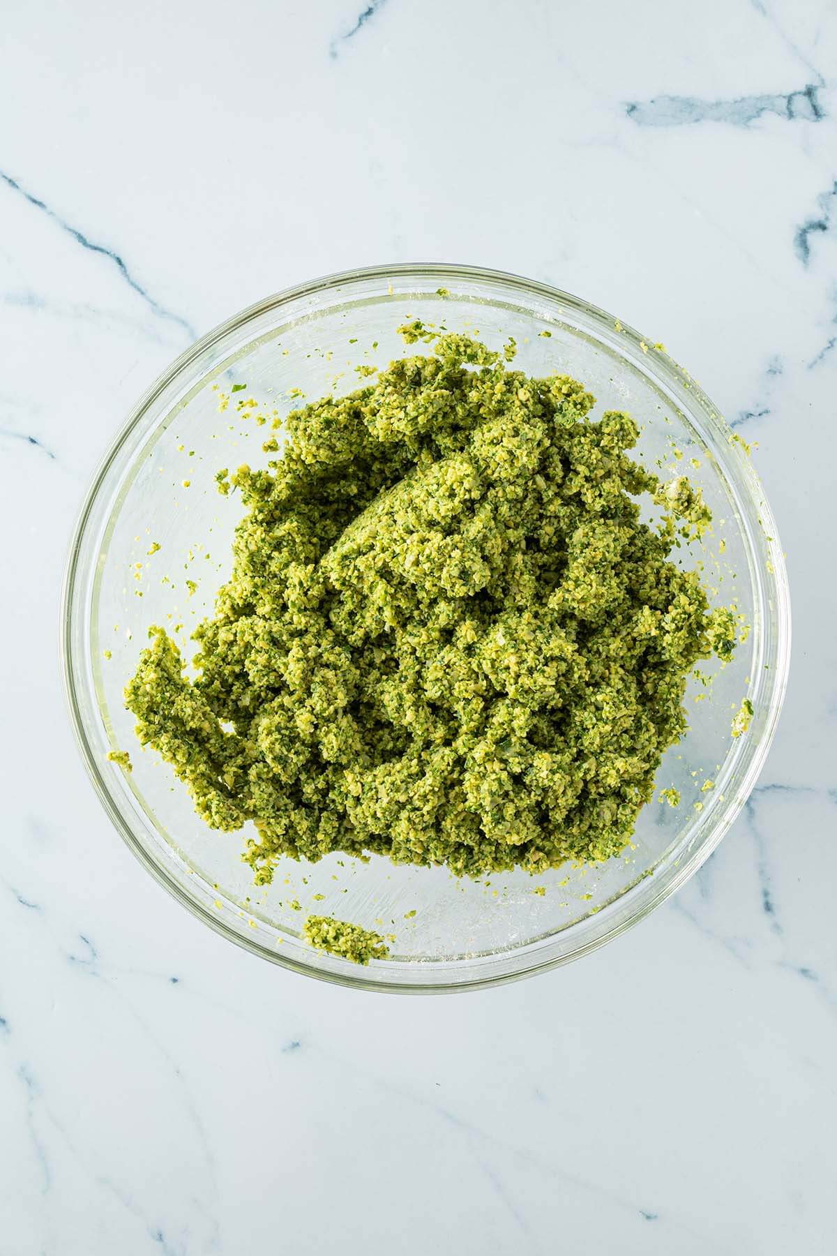 Fertiger Falafelteig in einer Glasschüssel, dessen Konsistenz an feuchten Sand erinnert.