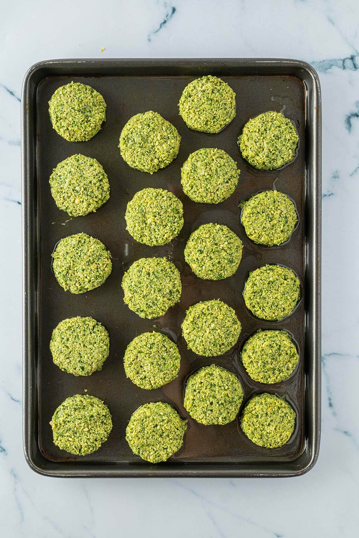 Vogelperspektive auf ein Blech mit 20 kleinen, rohen Falafel.