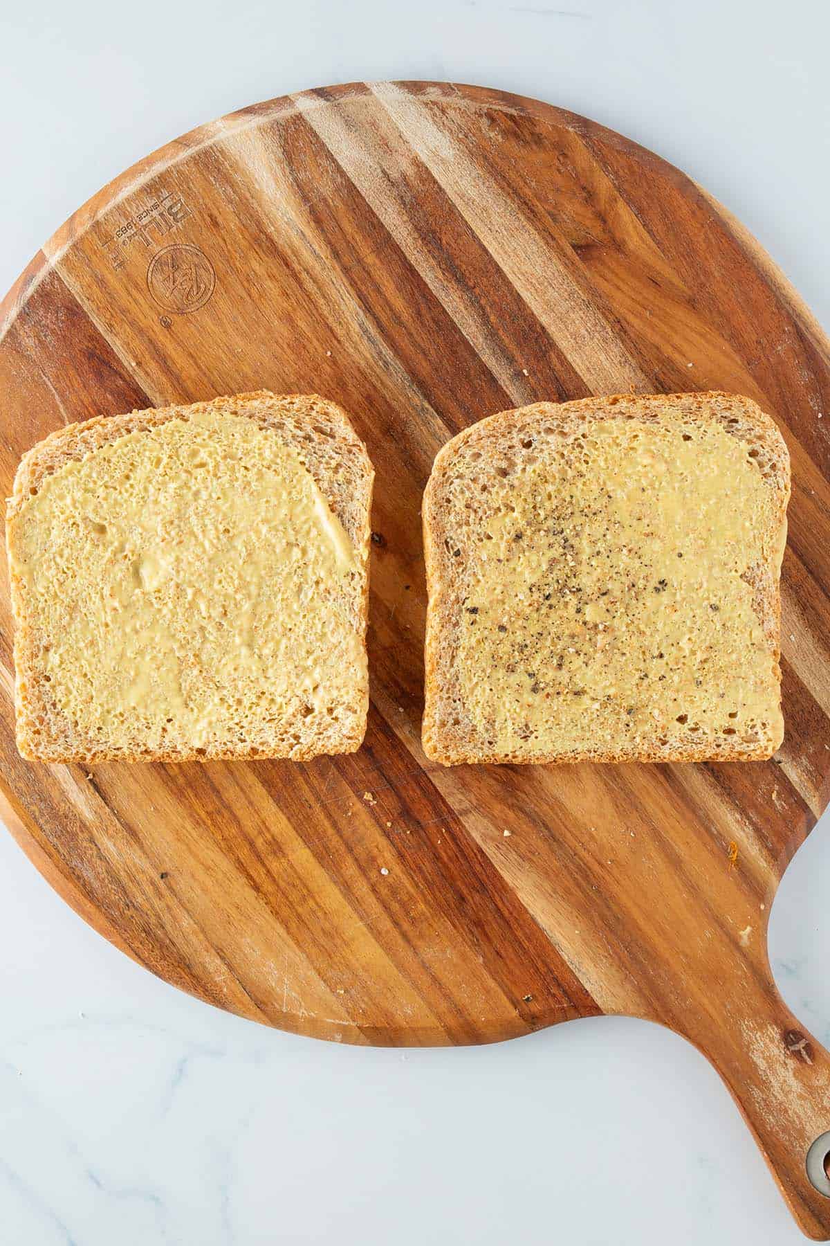 Zwei mit Senf bestrichene Toast Scheiben auf einem Brett.