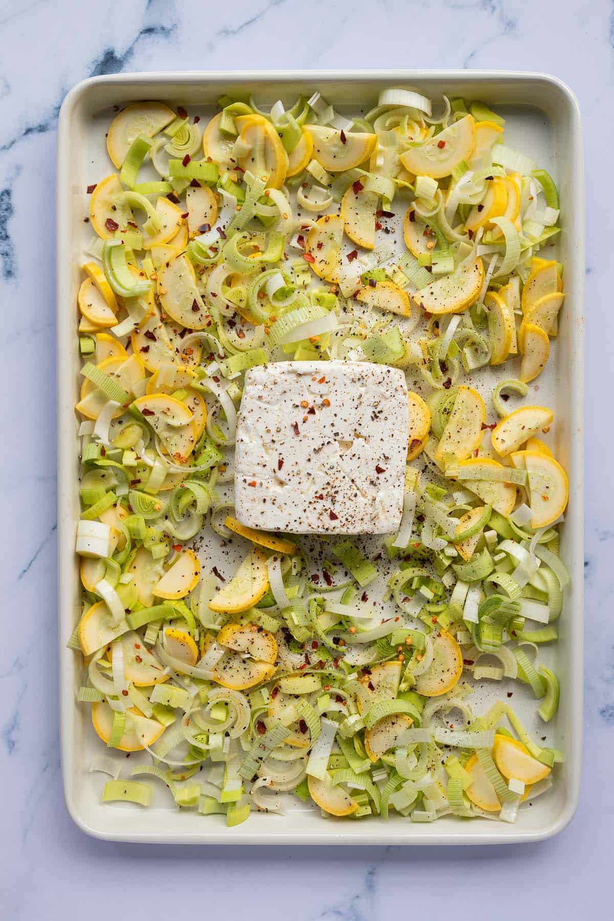 Ein Blech mit geschnittenem Gem&uuml;se und einem Block Feta.