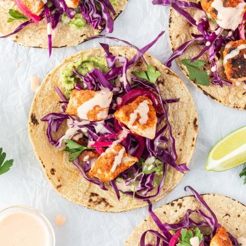 Vier mexikanische Fisch-Tacos auf wei&szlig;em Untergrund mit Limetten und Sauce.