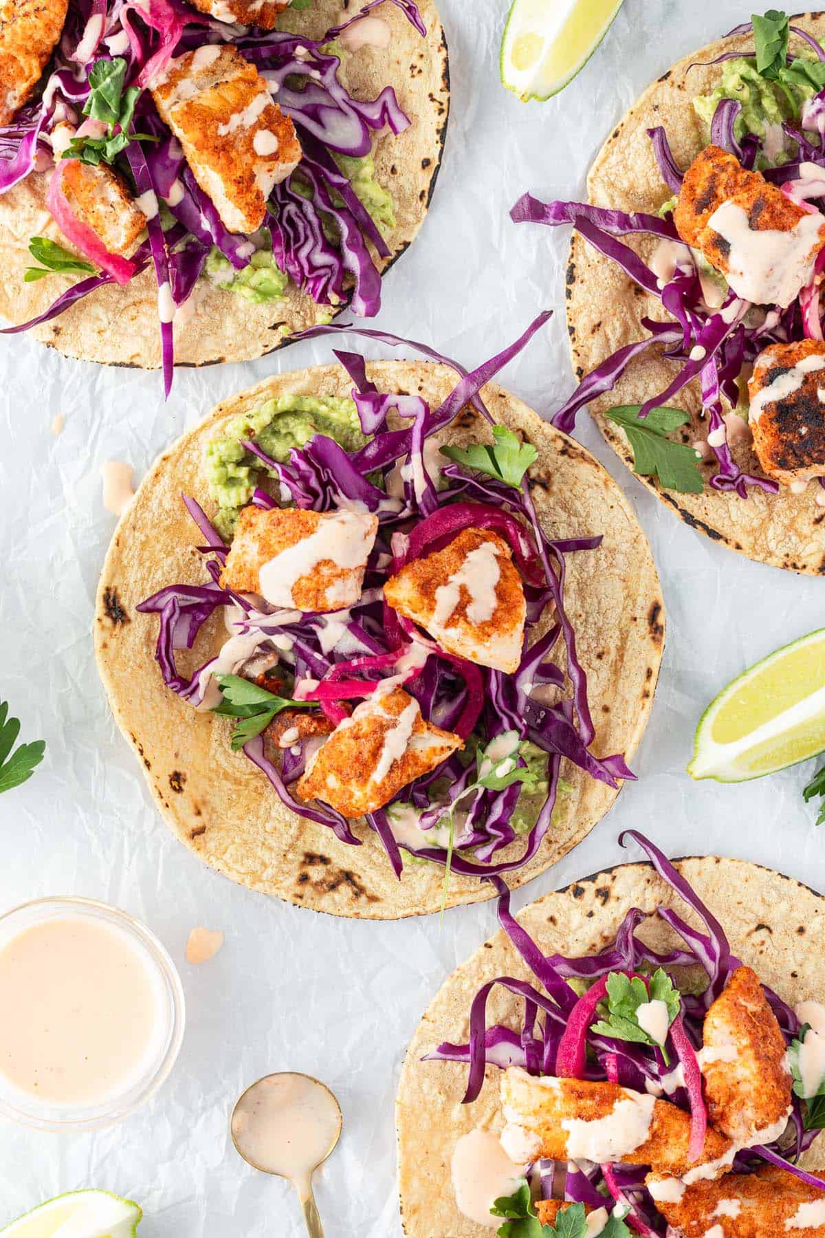 Vier mexikanische Fisch-Tacos auf wei&szlig;em Untergrund mit Limetten und Sauce.