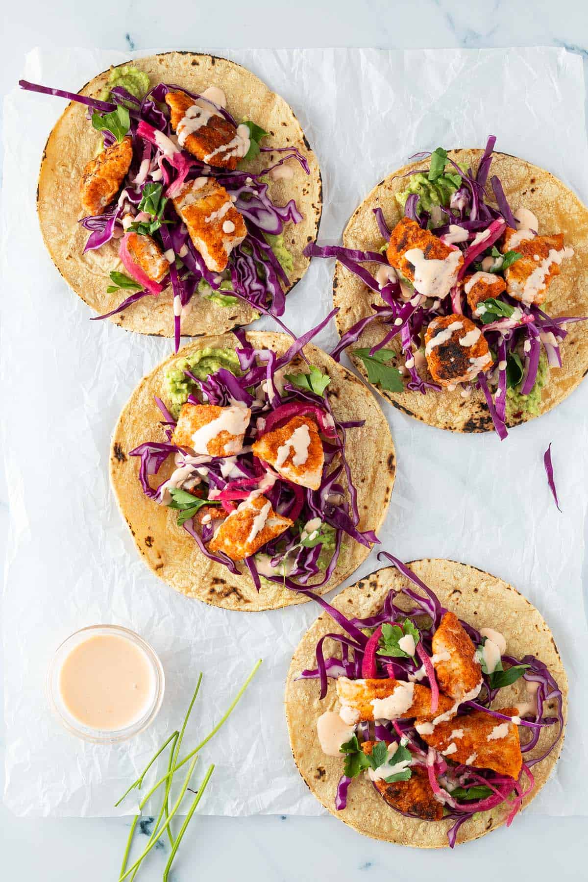 Vier fertig belegte Fisch Tacos mit Rotkohl, Zwiebeln, und Sauce.