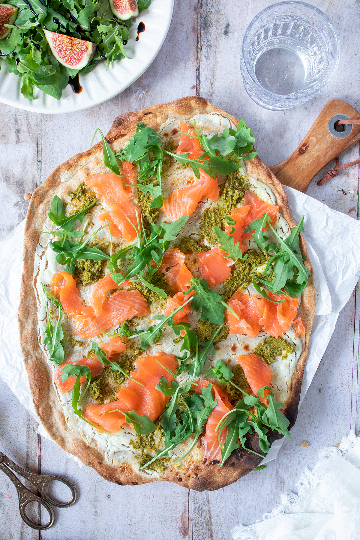 Knuspriger Flammkuchen mit Lachs, Rucola und Pesto auf einem Holzbrett serviert.