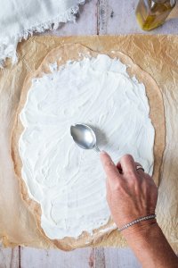 Flammkuchenteig wird mit Frischk&auml;se bestrichen.