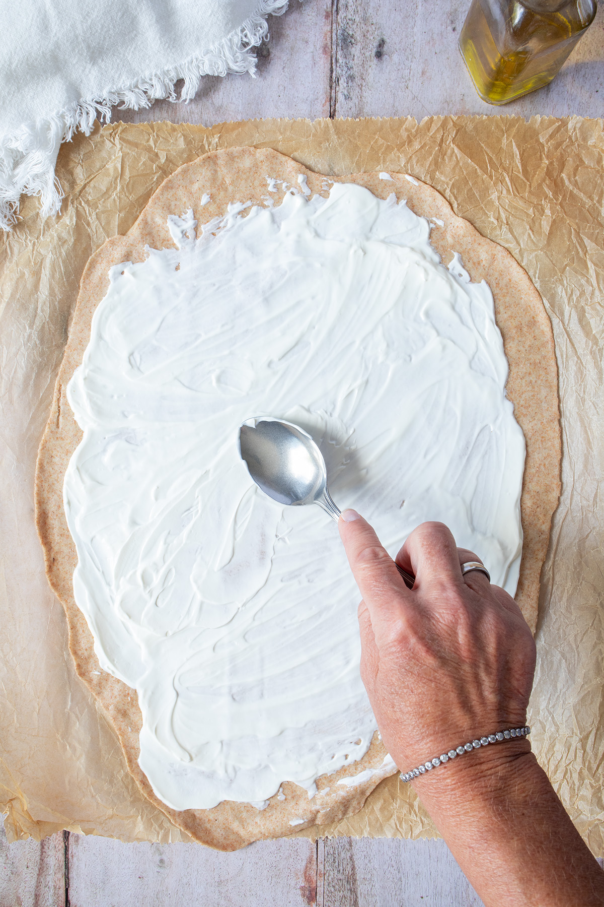 Flammkuchenteig wird mit Frischk&auml;se bestrichen.